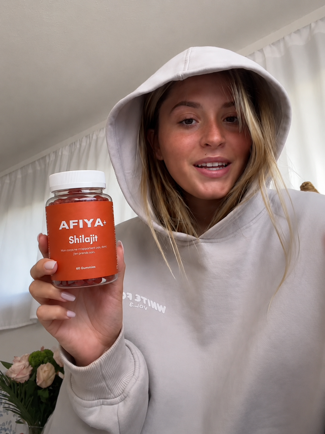 Cliente en hoodie présentant un flacon Afiya+ Shilajit chez elle
